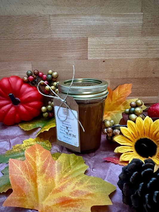 Pumpkin Spice Caramel – Fall Limited Edition in a mason jar with rustic tag, surrounded by autumn leaves, pinecones, and pumpkins for seasonal appeal.