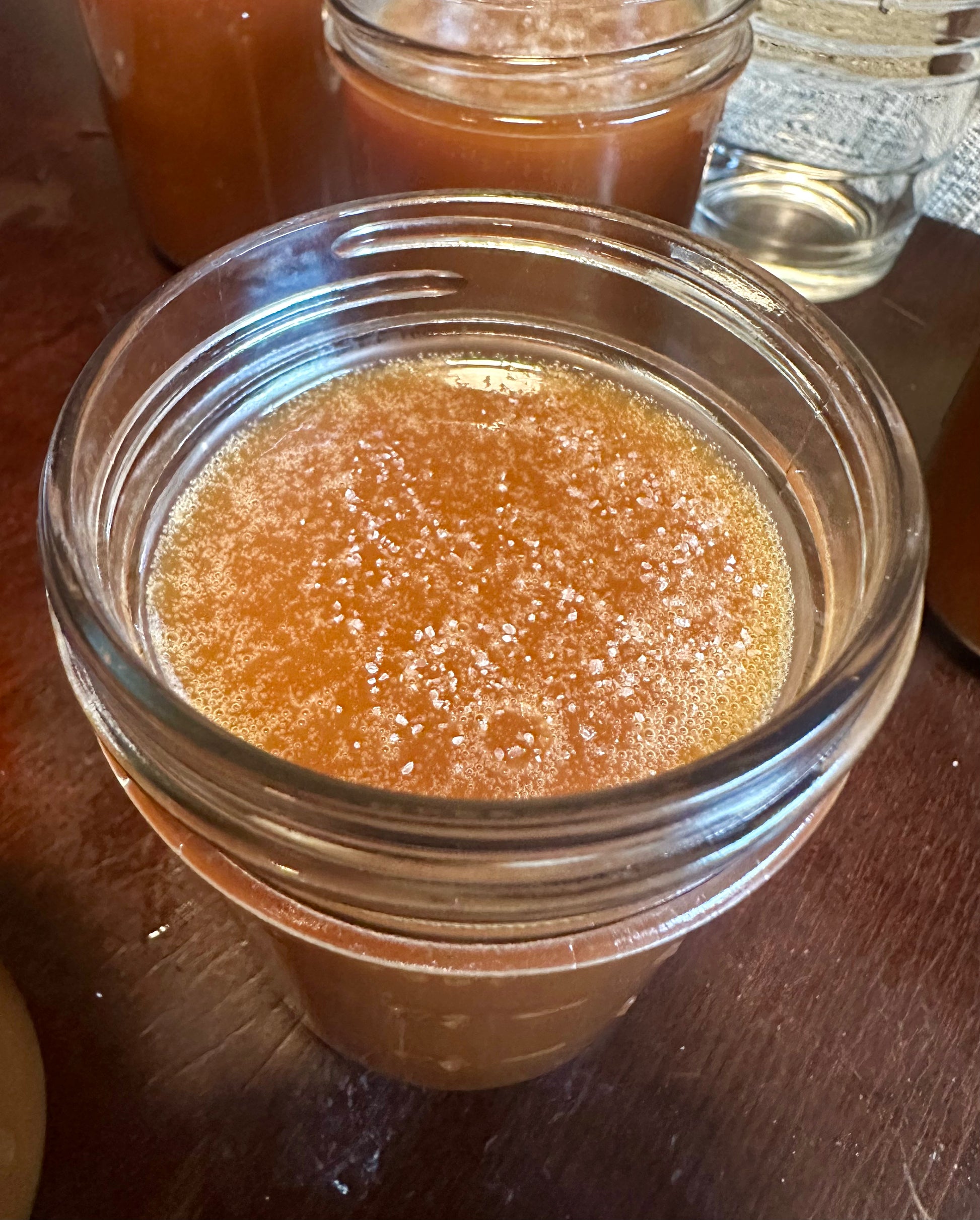 Open jar of Small Batch Salted Caramel Sauce showing rich, golden texture with sea salt crystals, ideal for gourmet dessert and coffee topping.